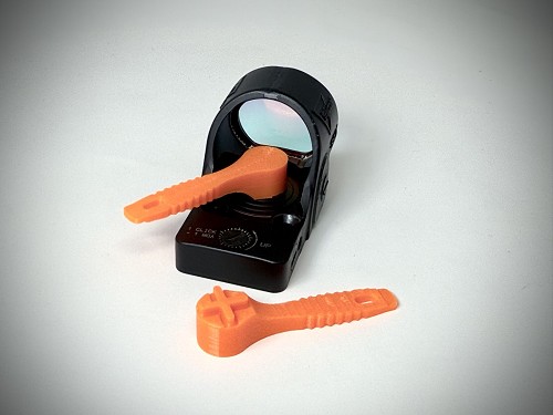 Bright orange Stonebridge Gunworks SRO Battery Tool V2 seated on a Trijicon SRO battery cap, with a second tool lying beside the optic 